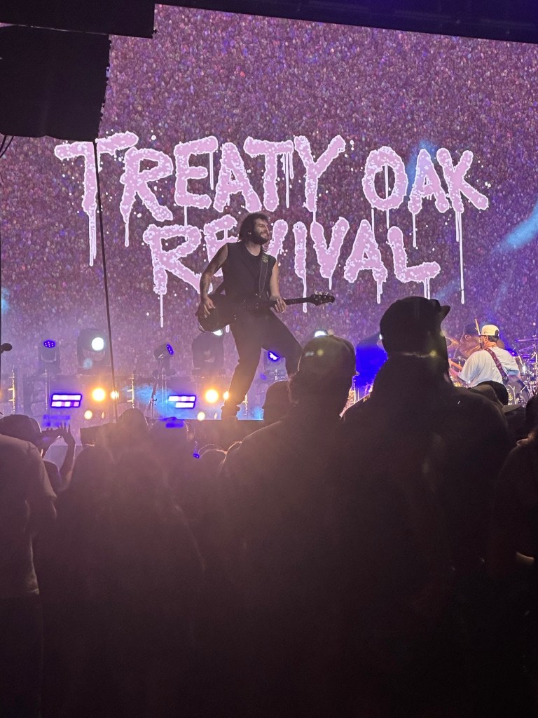 Treaty Oak Revival performing onstage with colorful concert lighting and audience silhouettes.